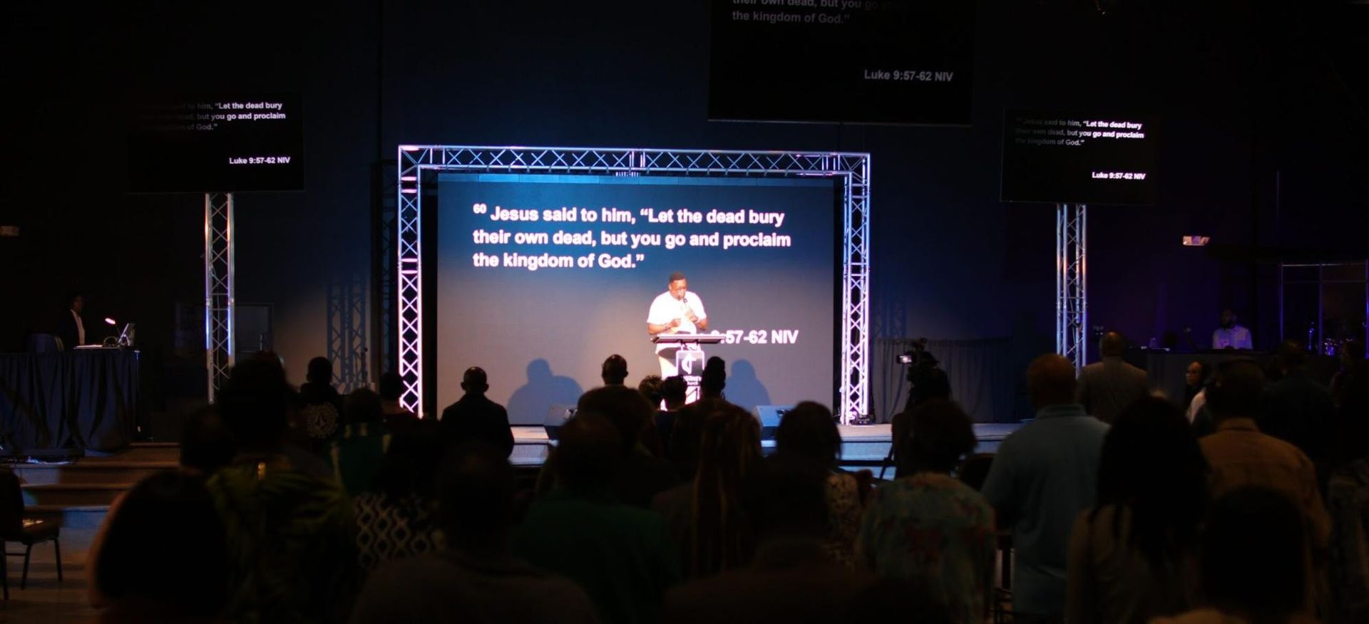 A man is giving a speech in front of a large screen