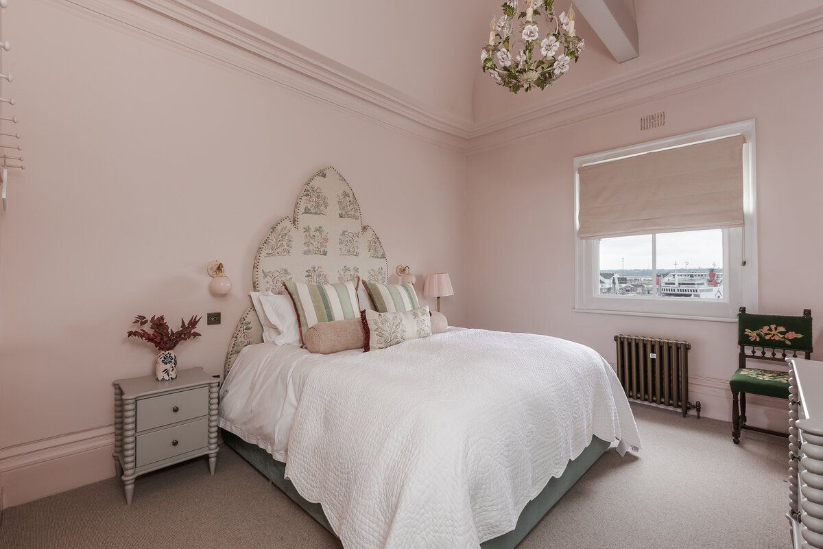 A bedroom with pink walls and a white bed.