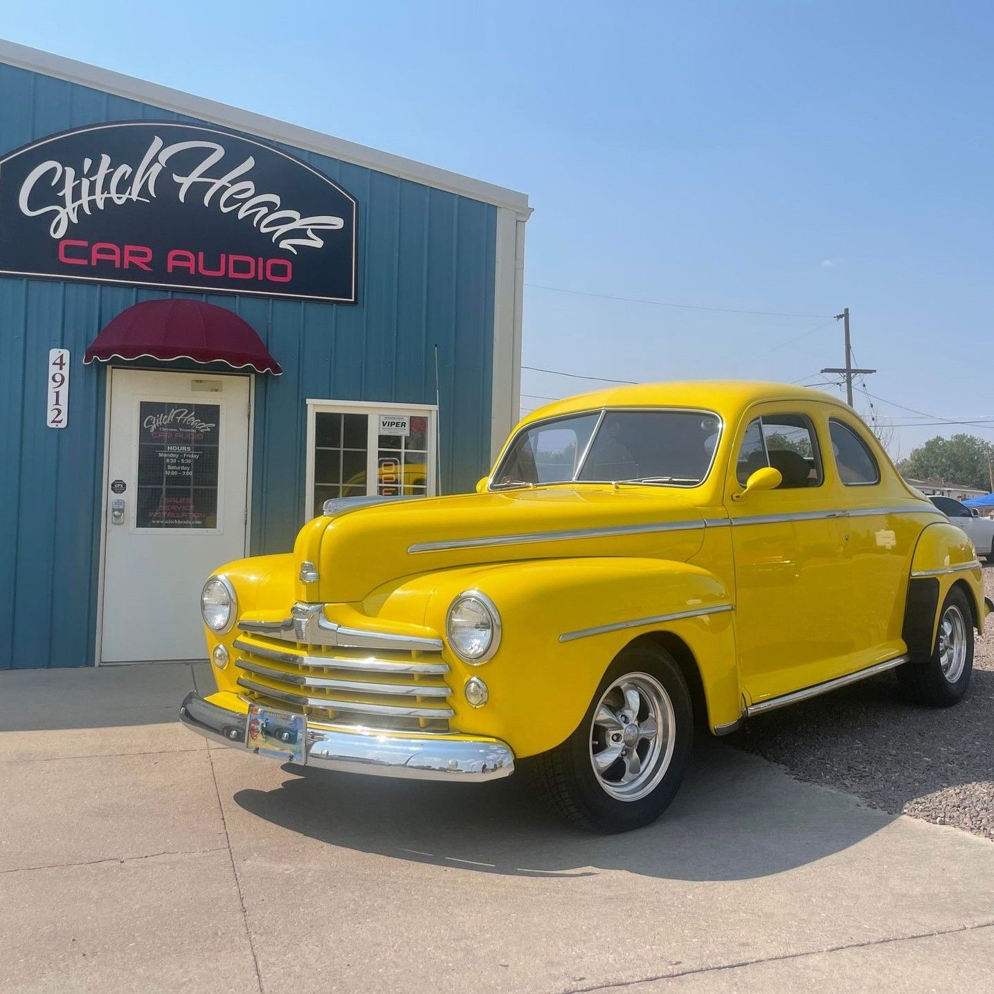 A yellow car is parked in front of a store called glitch hearts car audio