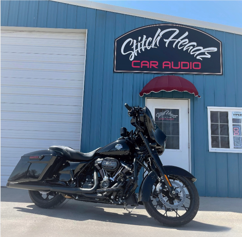 A black motorcycle is parked in front of a building that says stitch heads car audio
