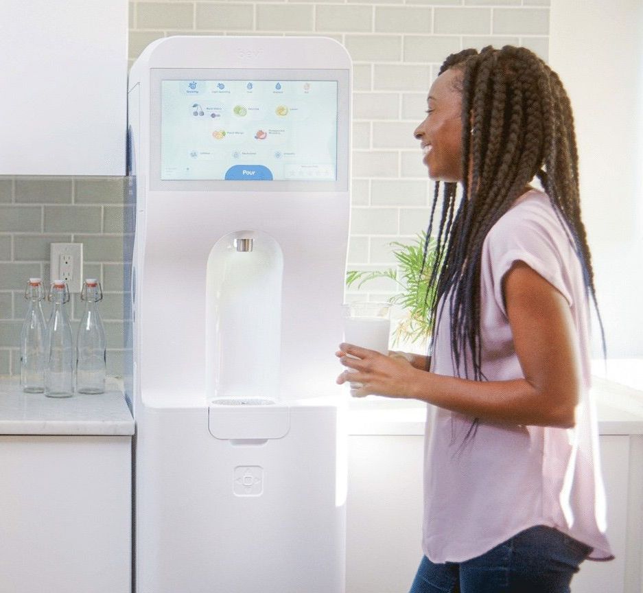 A woman is standing in front of a water dispenser in a kitchen.