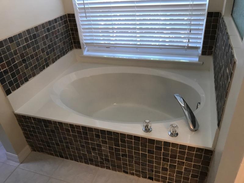 A bathtub in a bathroom next to a window with blinds