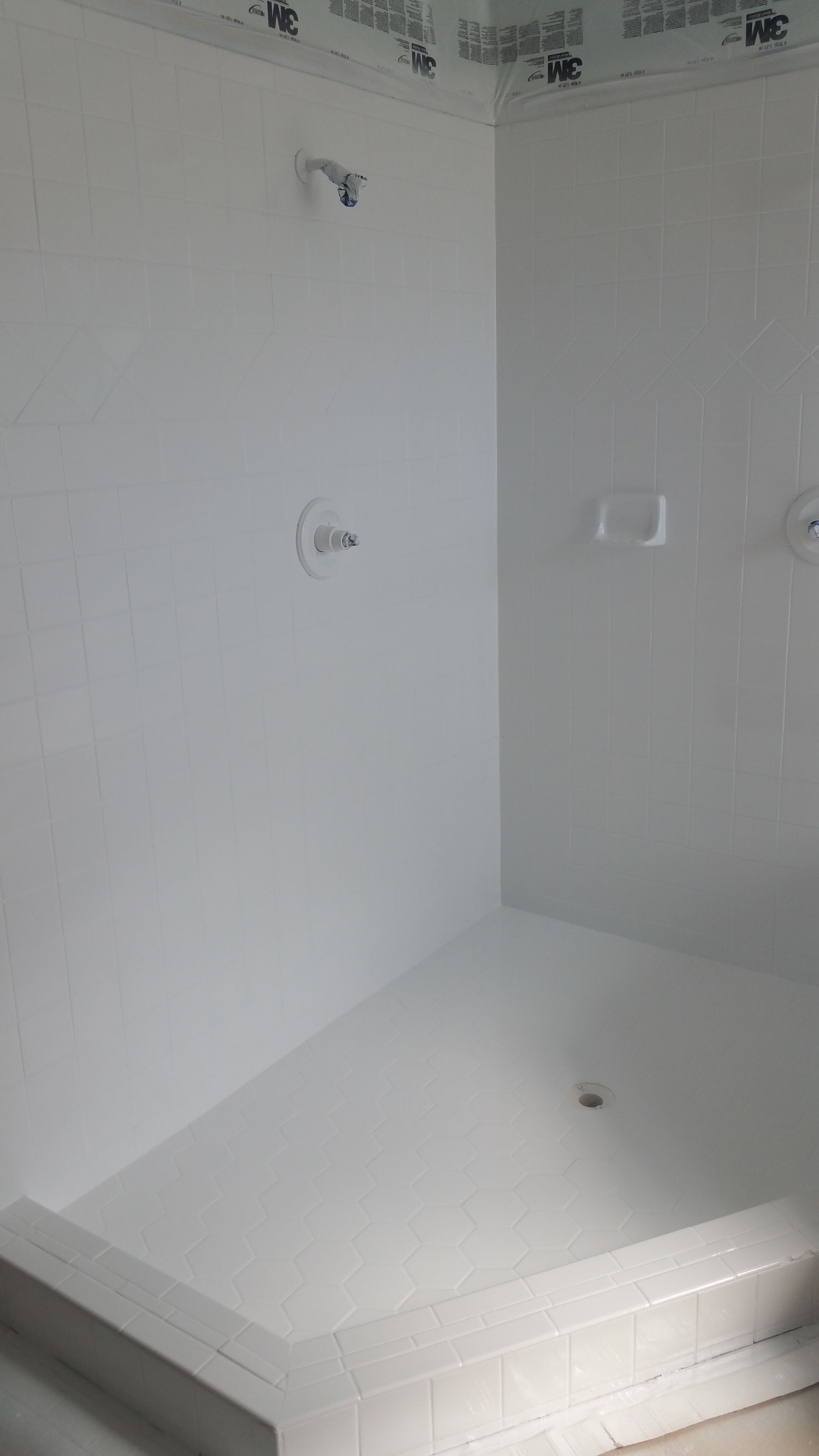 A shower stall in a bathroom with white tiles and a shower head.