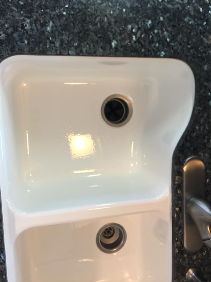 A white sink with two drains on a black counter top.