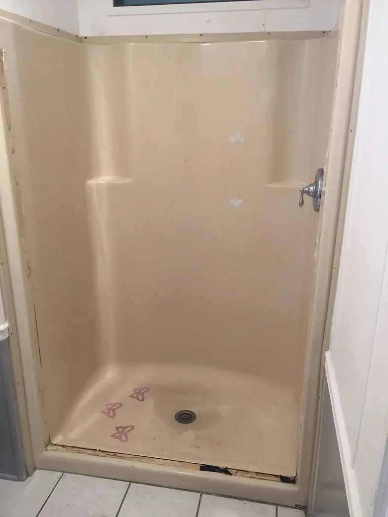 A beige shower stall in a bathroom with a drain.