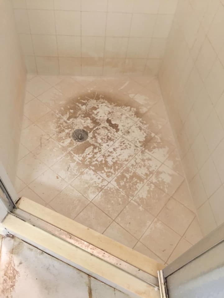A dirty shower stall with a drain in the middle of it.