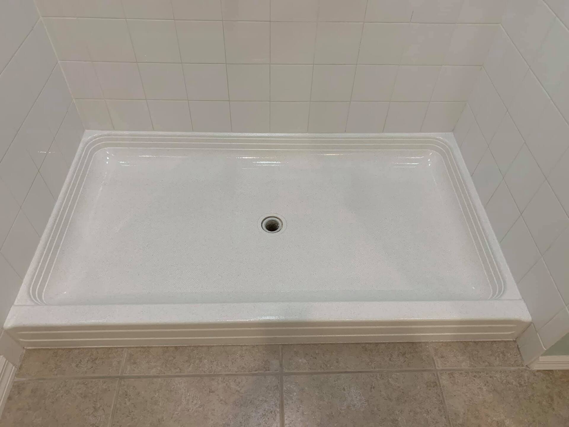 A white shower stall with a drain in a bathroom.