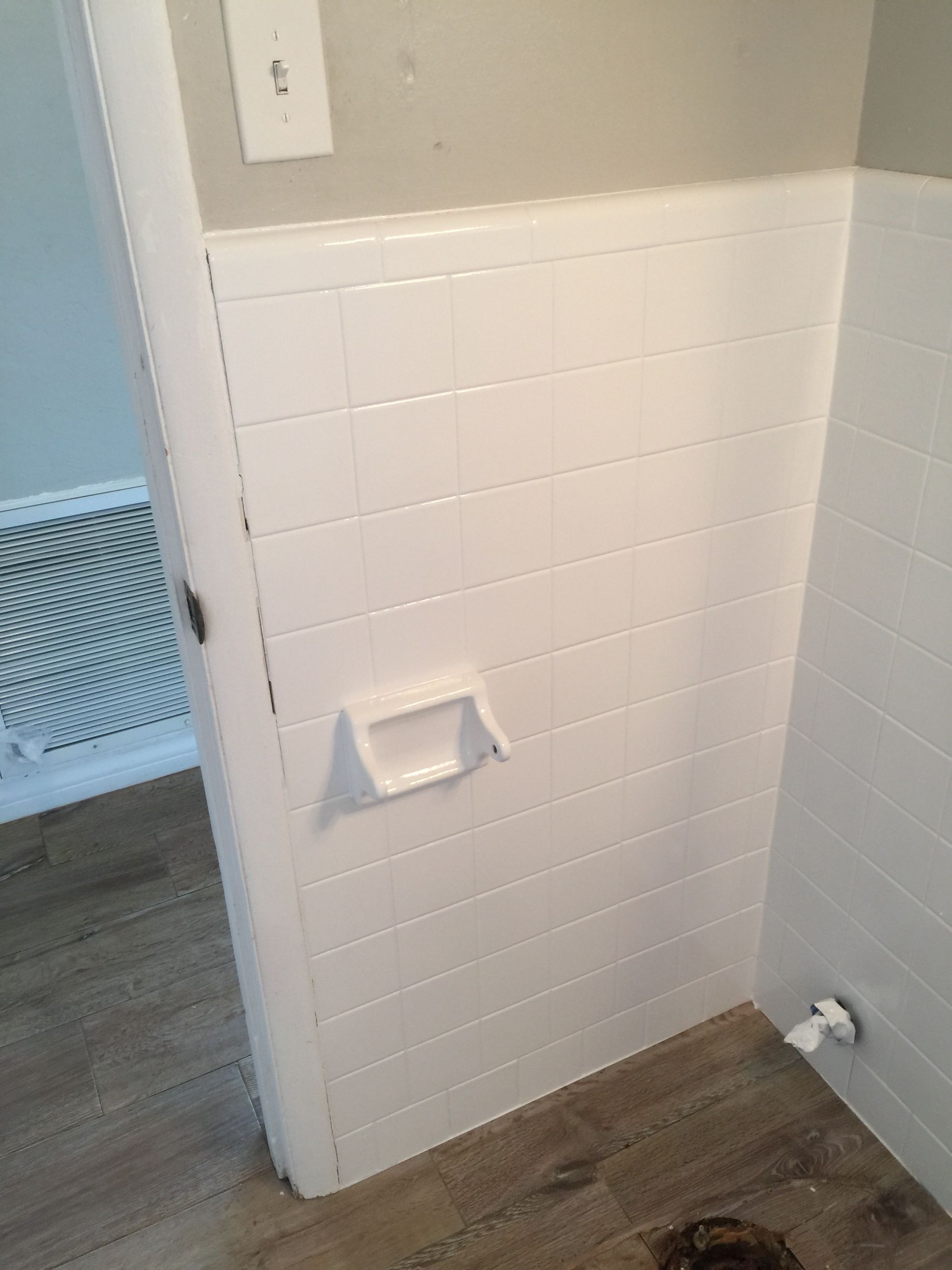 A bathroom with white tiles and a toilet paper holder on the wall.