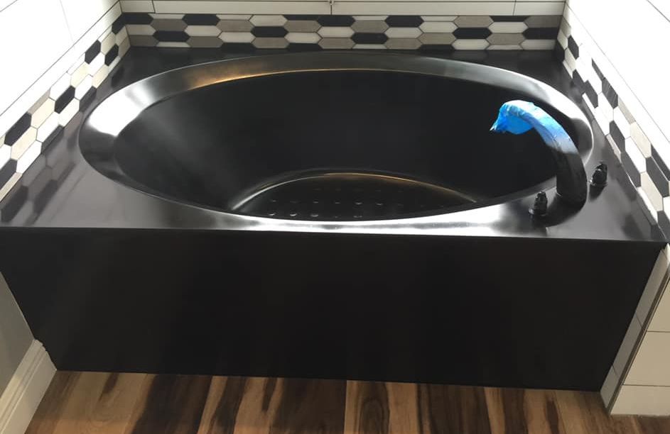 A black bathtub is sitting on a wooden floor in a bathroom.