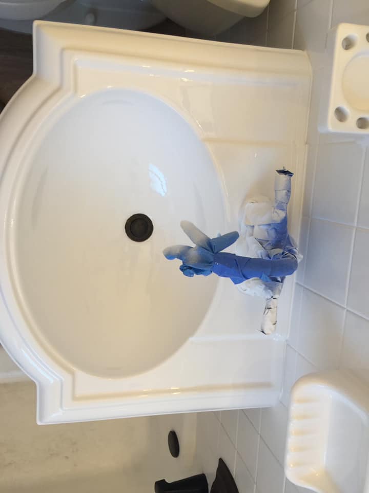 A white bathroom sink with blue gloves on the faucet