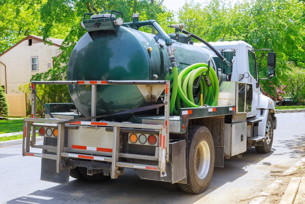 Vacuum truck with large tank and green hose parked on a leafy residential street