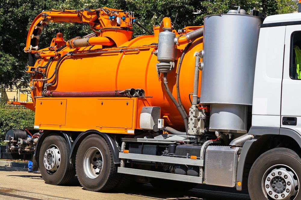 Orange vacuum truck with hose equipment parked on a street, side view