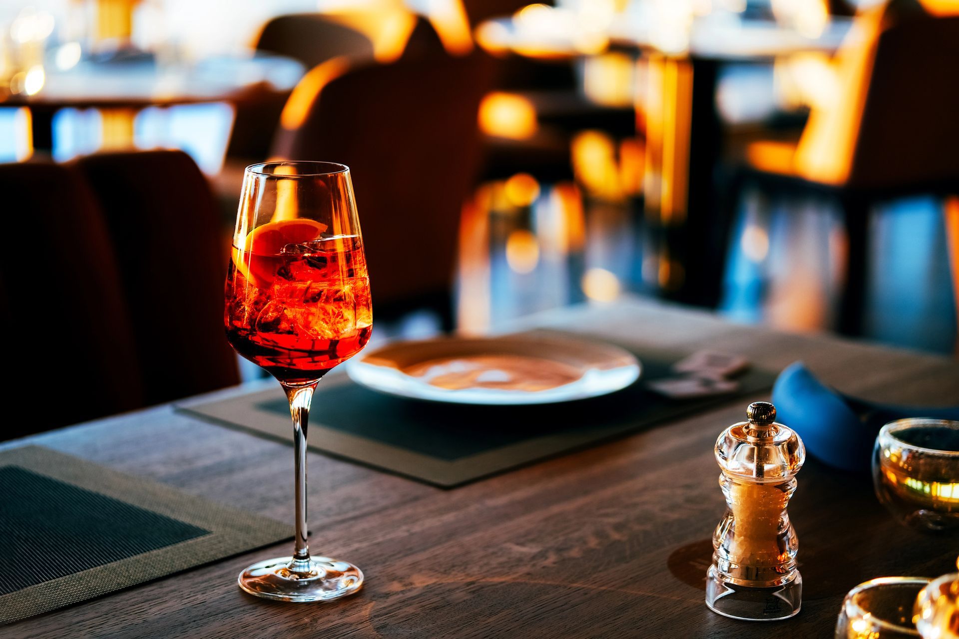 Cocktail rosso con una fetta d'arancia su un tavolo di un ristorante, sfondo sfocato con luce calda.