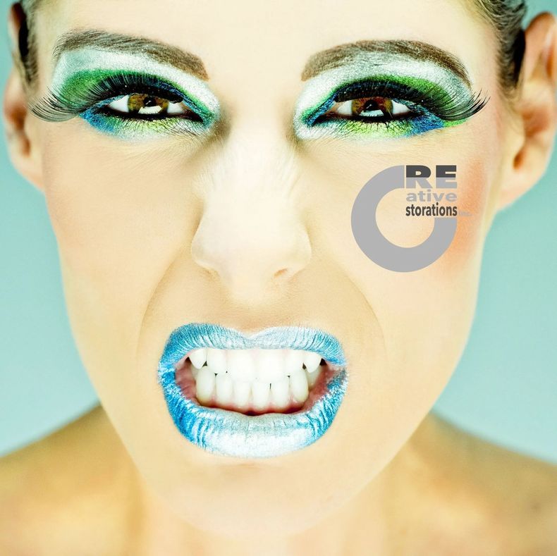 Woman with vibrant blue lipstick and eye makeup, open mouth. Gritting teeth, angry expression.
