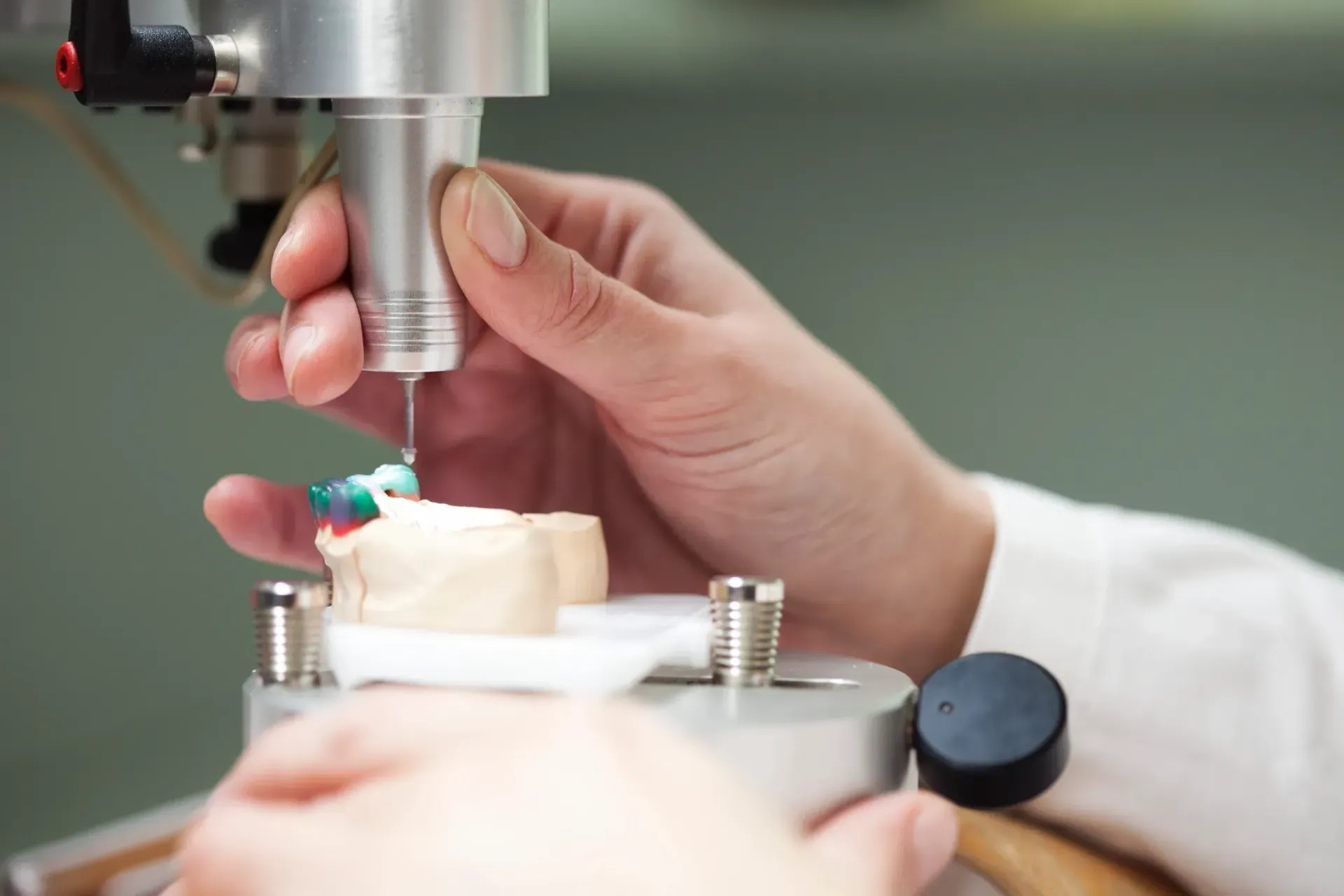 Person using a precision tool to work on a dental mold in a lab setting.