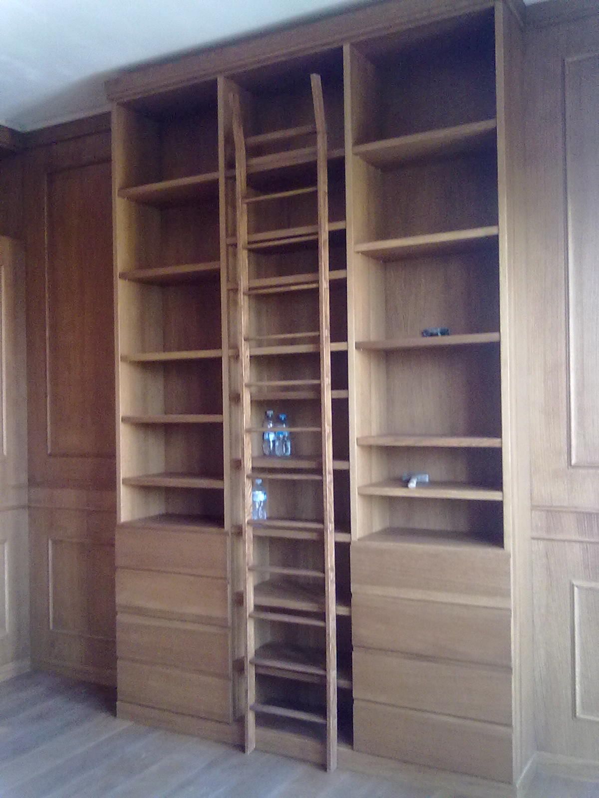 Una libreria in legno a tutta altezza con tre sezioni principali, al cui centro si trova una scala a rotelle da biblioteca.