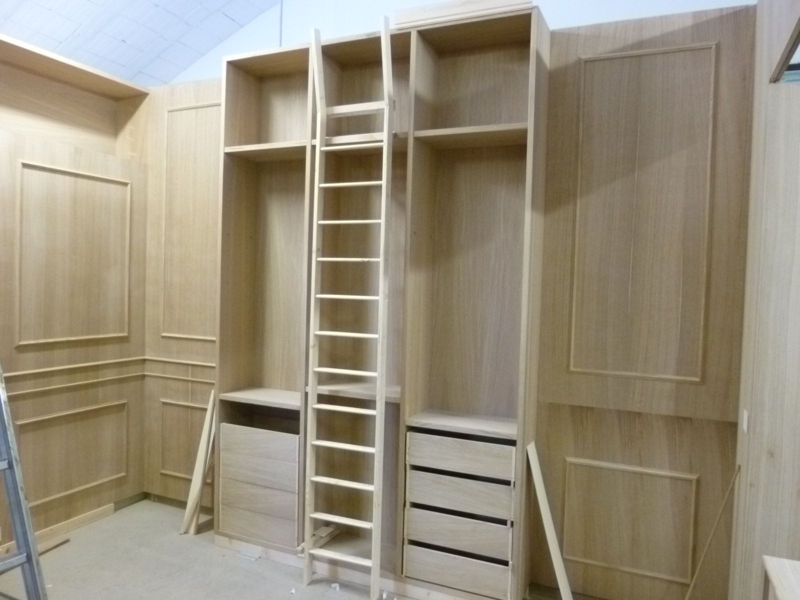 Armadi a muro e scaffalature in legno chiaro non rifinito con scala scorrevole in una stanza con pannellatura a parete coordinata.