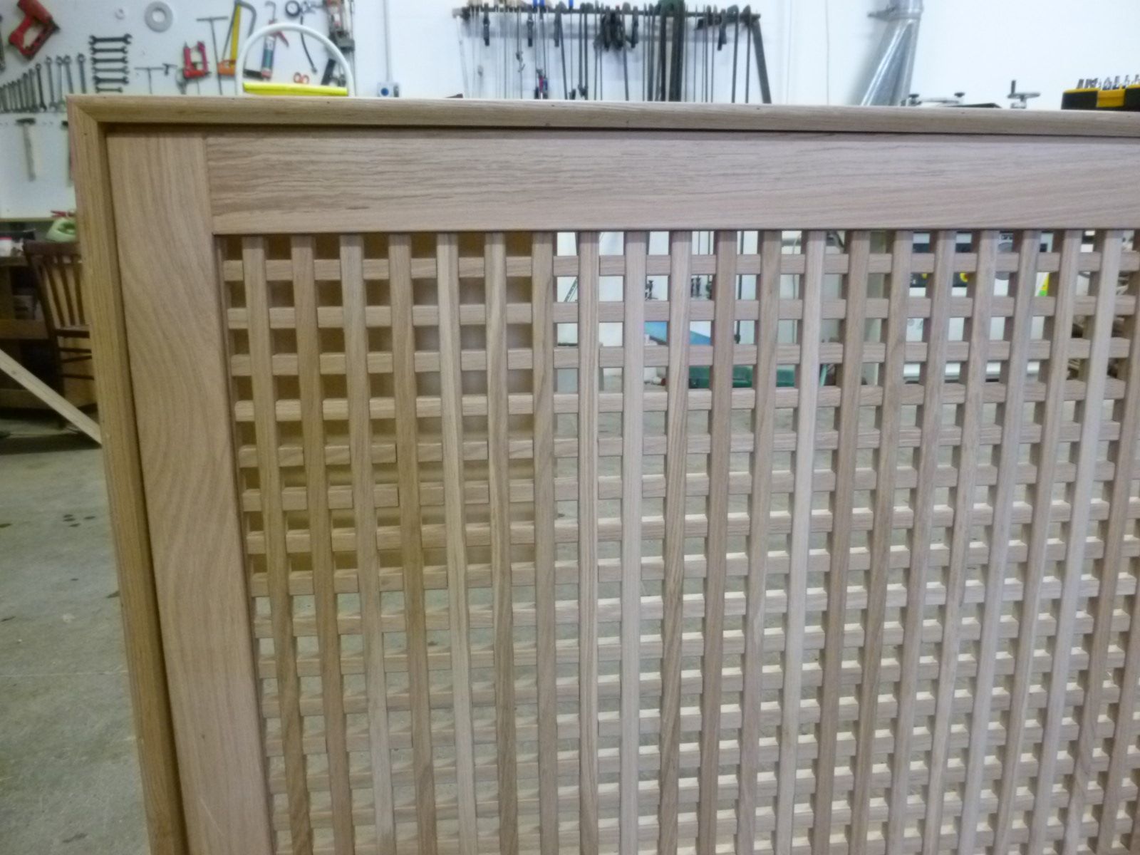 Primo piano di una copertura in legno per termosifone con motivo a griglia quadrata, ambientata in una falegnameria.