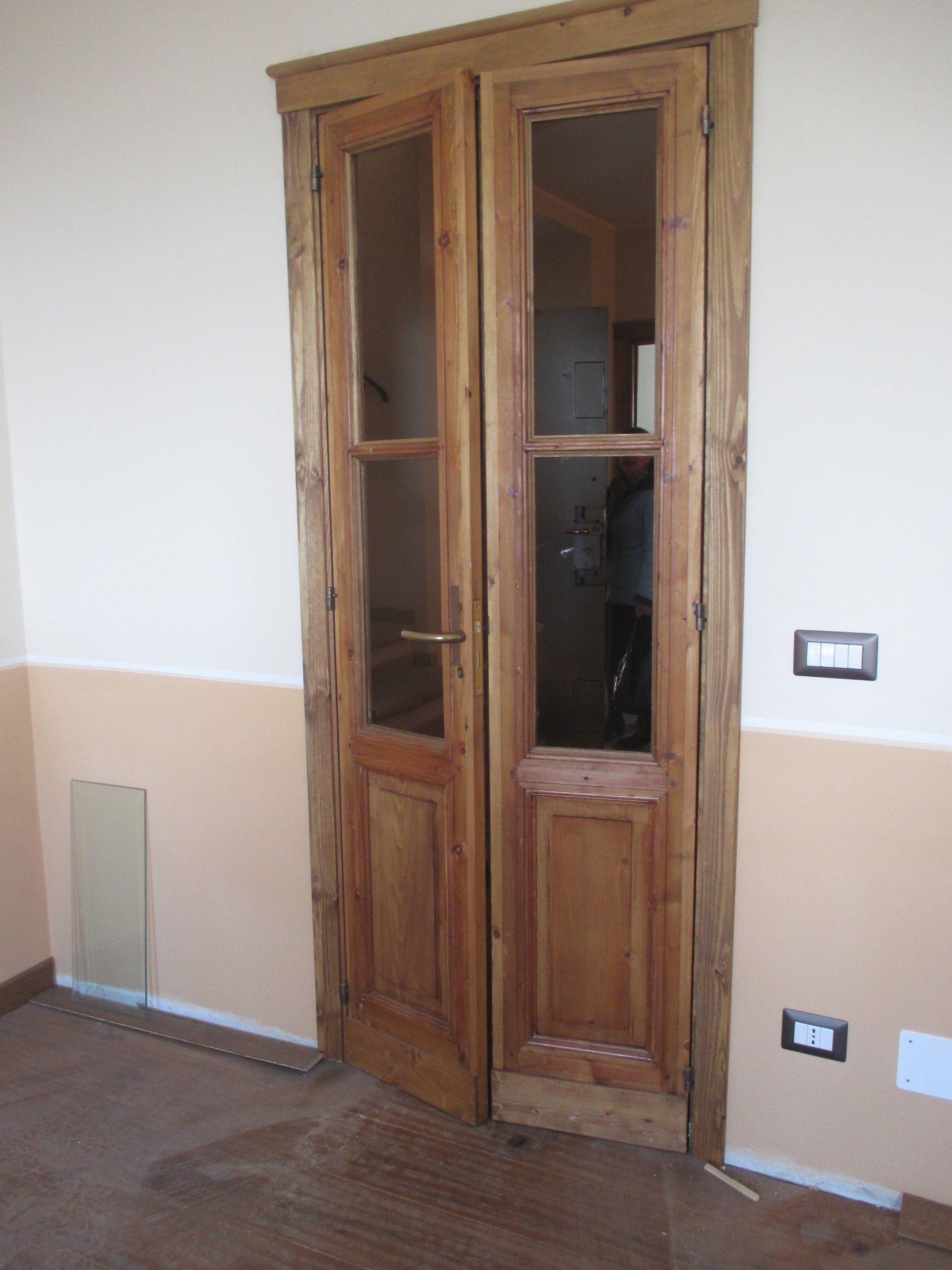 Doppie porte con telaio in legno e pannelli in vetro in una stanza interna con pareti color crema e pesca.