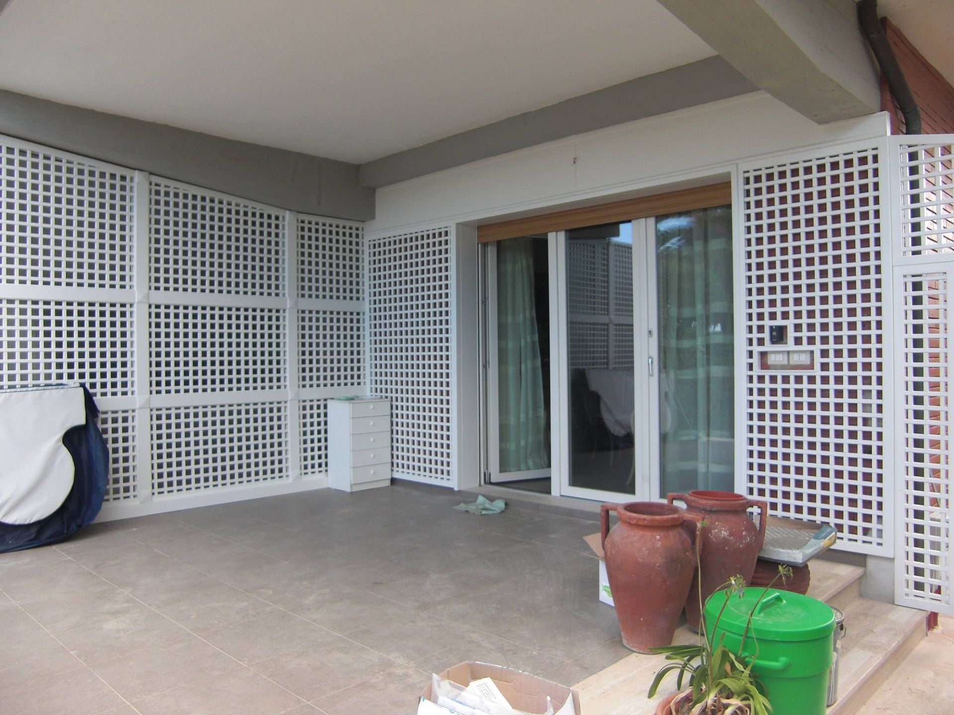 Su un patio esterno, accanto a una porta scorrevole in vetro, si trova un paravento in legno bianco a griglia.