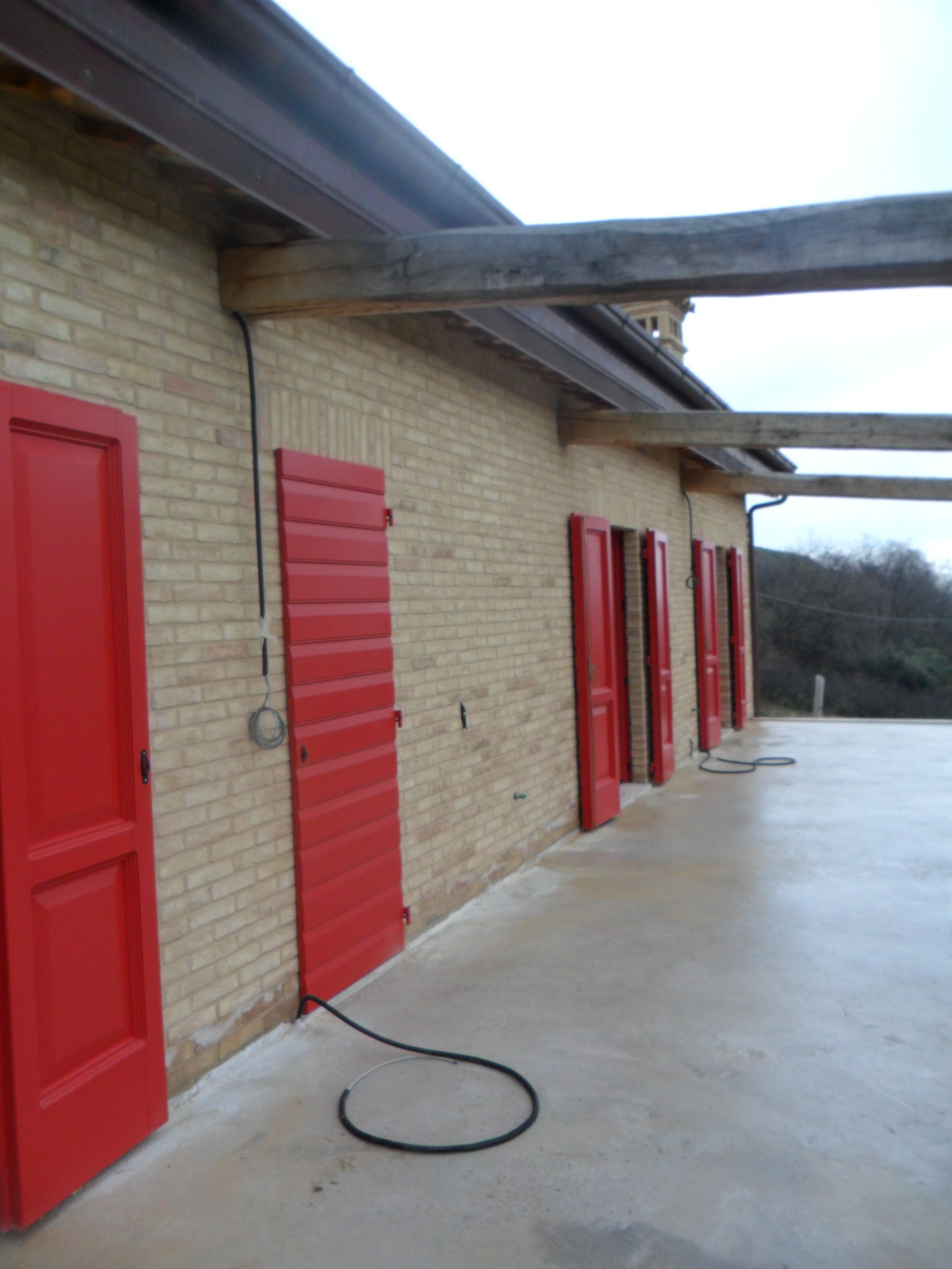 Una fila di porte rosso acceso su un edificio in mattoni color sabbia, con travi in ​​legno che si estendono su un patio in cemento.