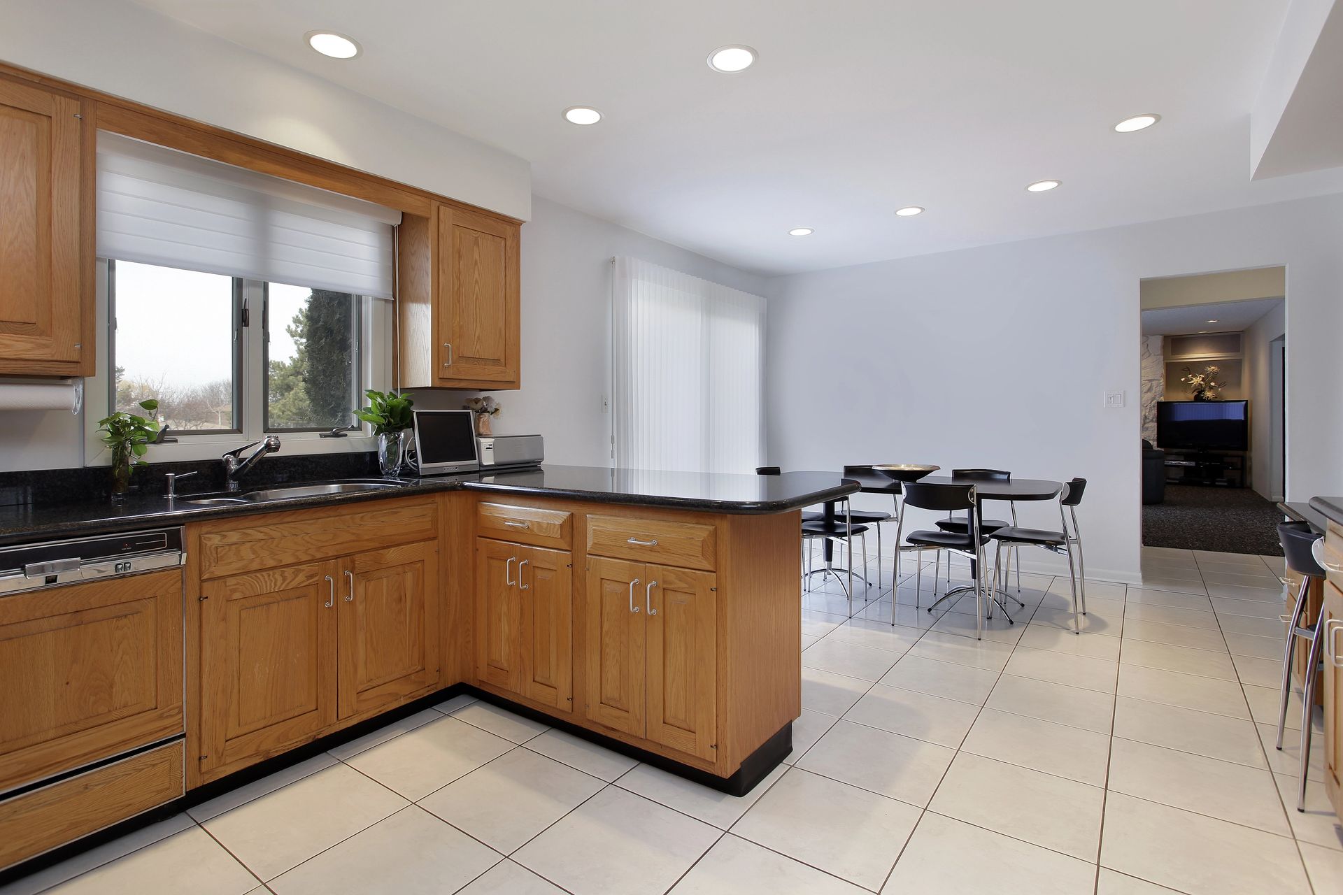 Cucina con mobili in rovere, ripiani scuri e pavimento in piastrelle, che si apre su una zona pranzo con tavolo e sedie.