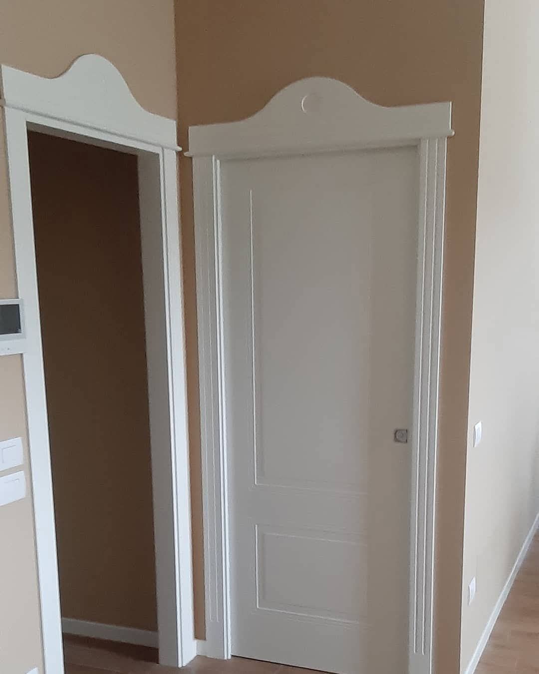 Due porte bianche con cornici in legno decorate ad arco, in contrasto con pareti color marrone chiaro.