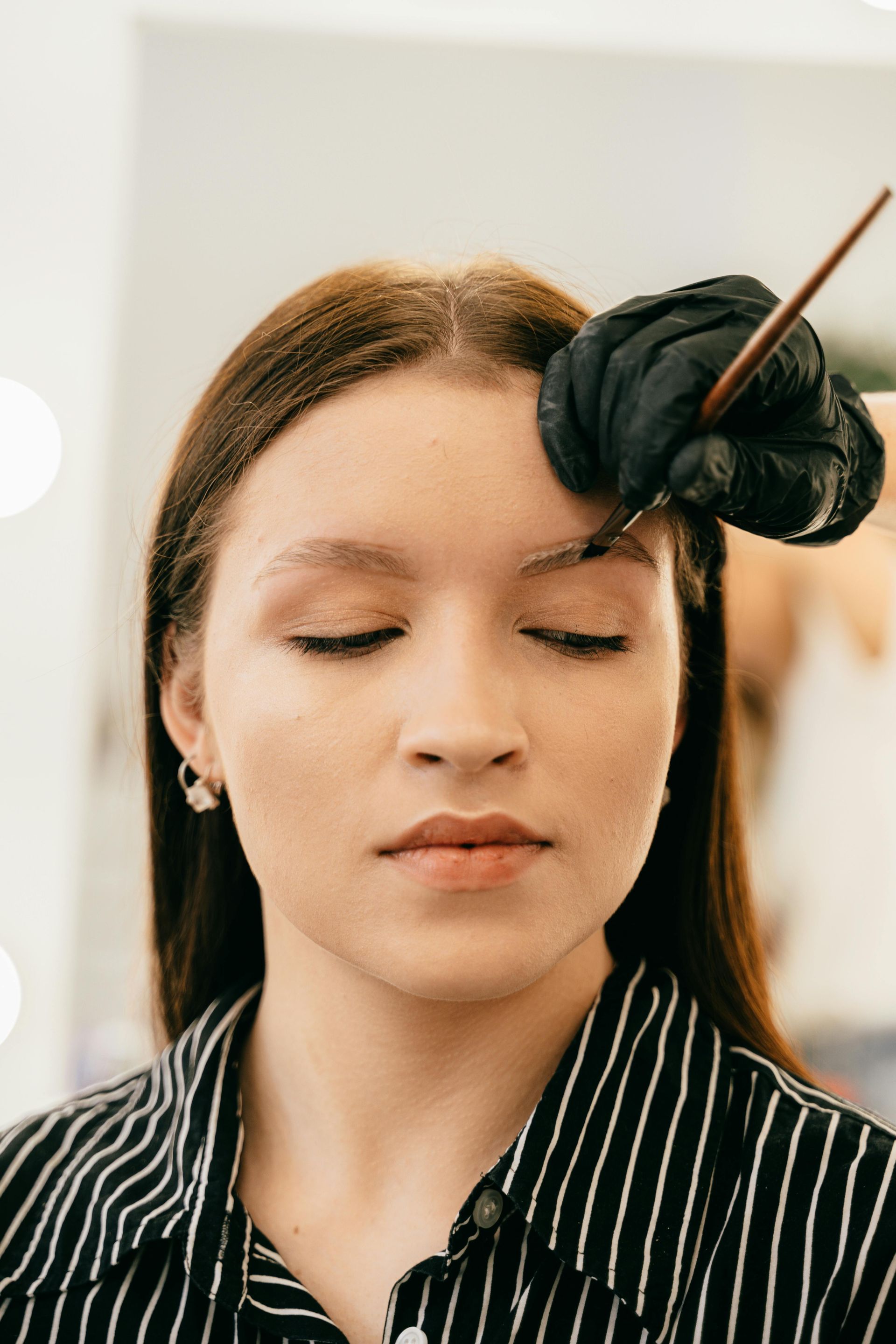 A person getting their eyebrow shaped by someone wearing a black glove.