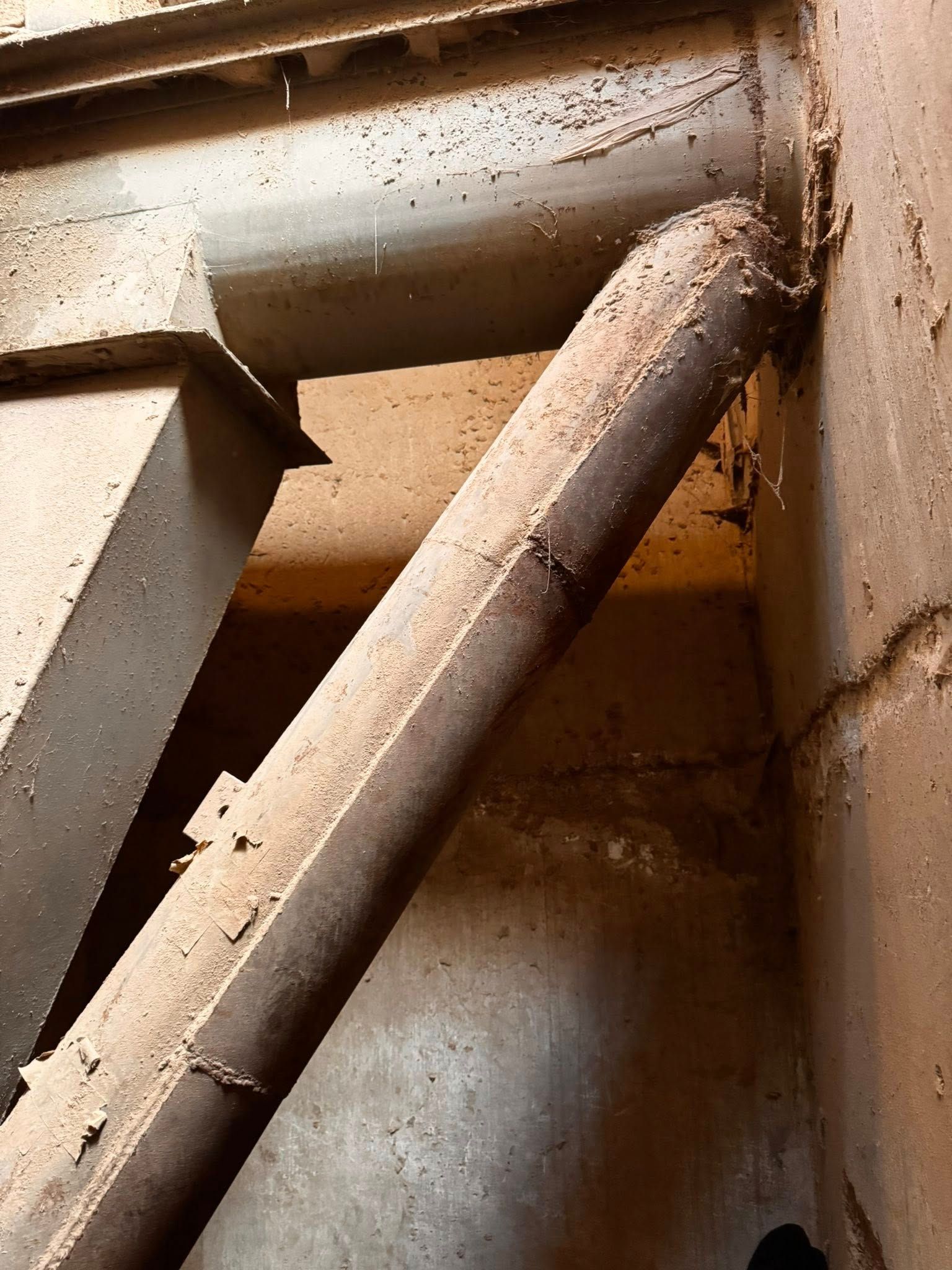Angled, rusty metal support beam against a dusty industrial wall.
