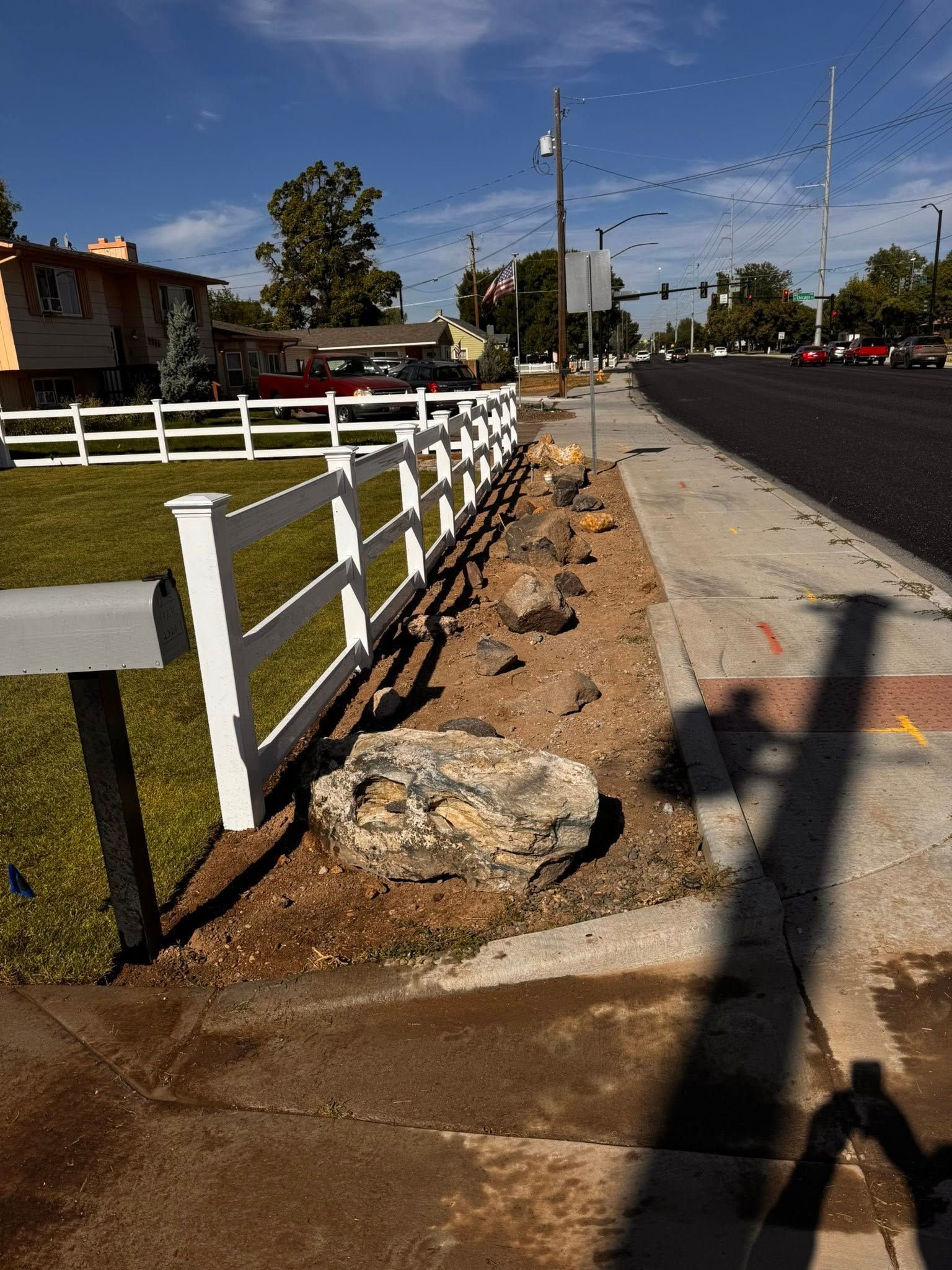 White fence in front yard with mailbox and rock border next to a road.