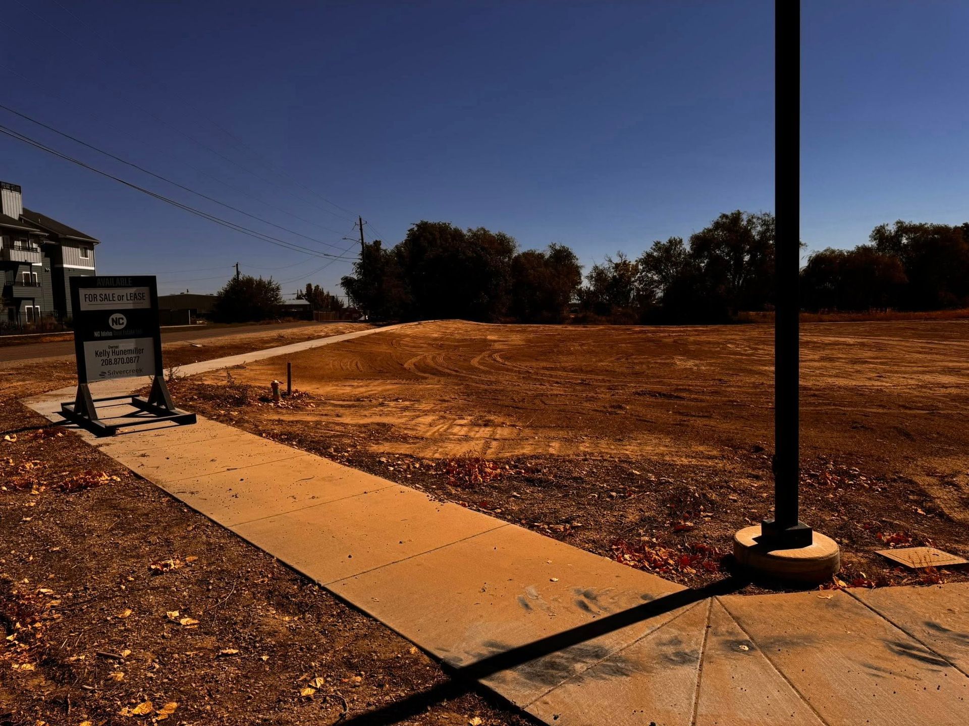 A vacant lot under a blue sky, with a walkway and sign, potentially for a construction site.