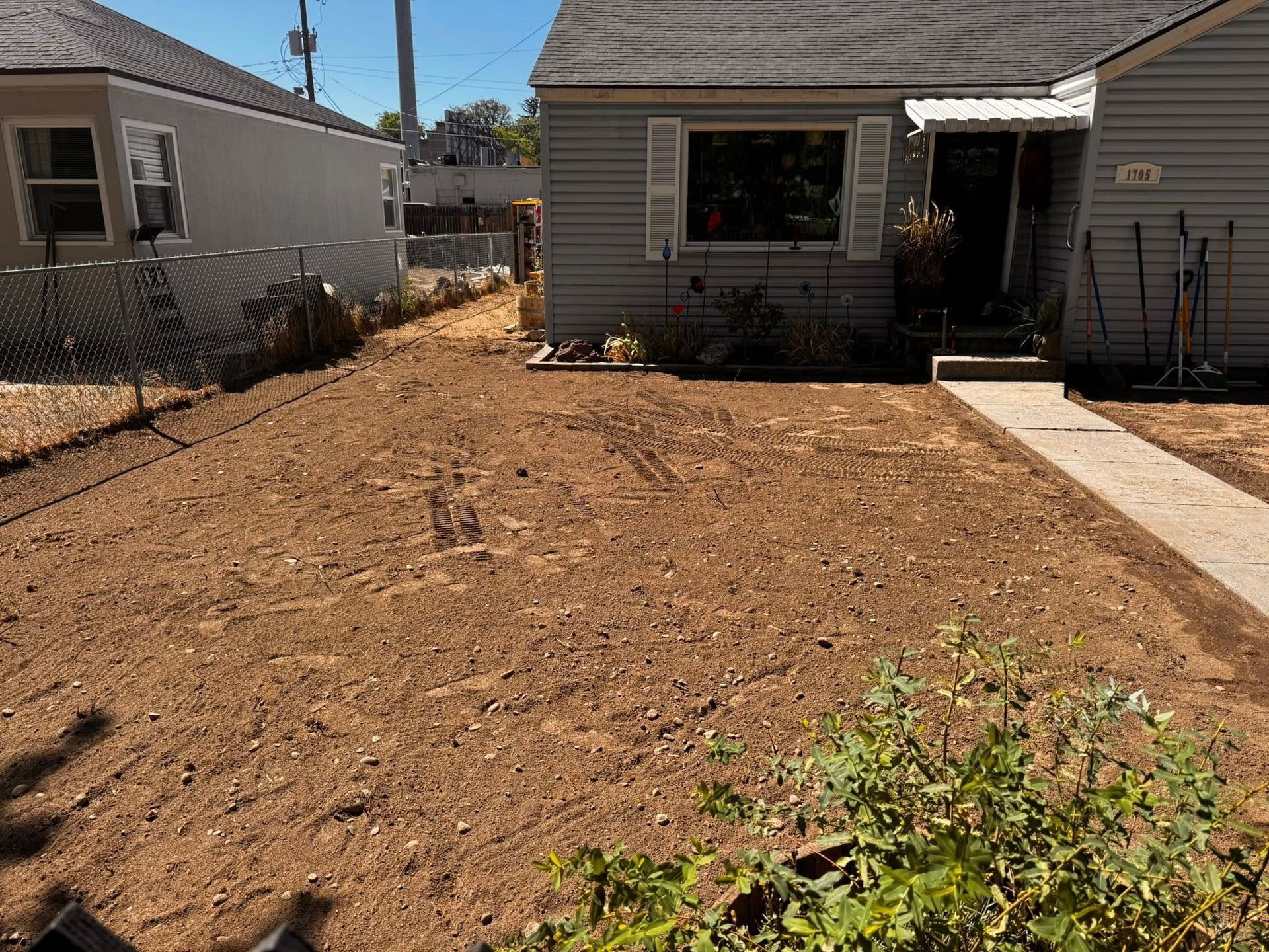 A house with a dirt front yard. A sidewalk leads to the front door. The sky is blue.