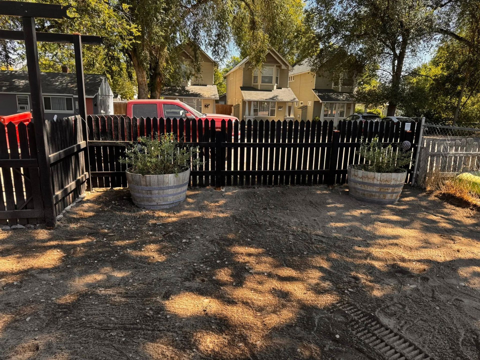 Wooden fence with planters, two houses in the background, trees casting shadows.