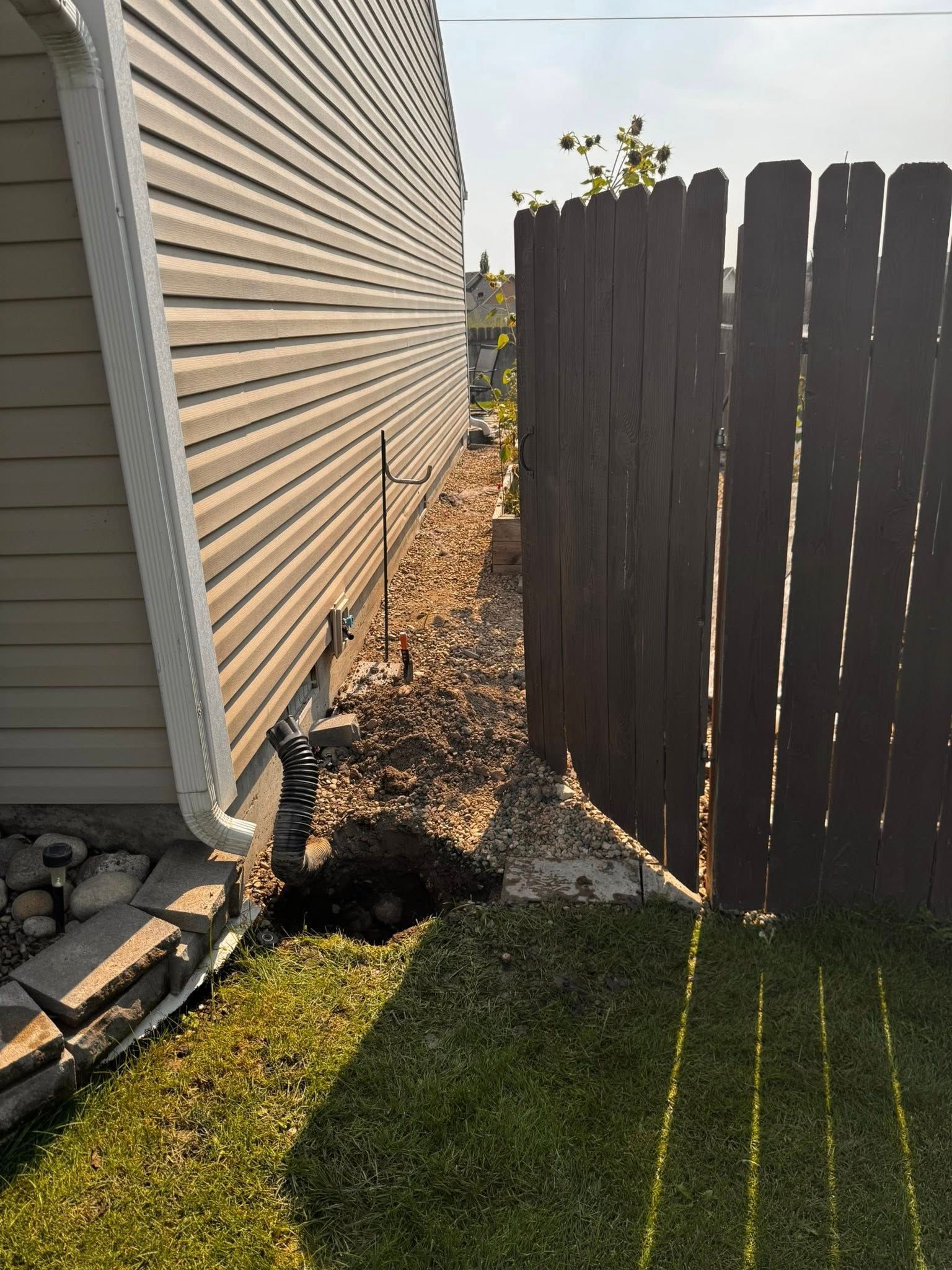 Side of house next to a brown fence; gravel and grass in between.