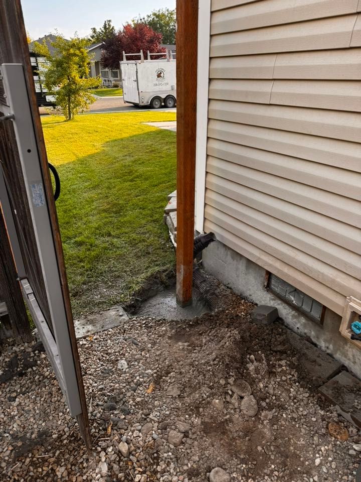 Brown wooden post next to beige house with dirt and gravel on the ground.