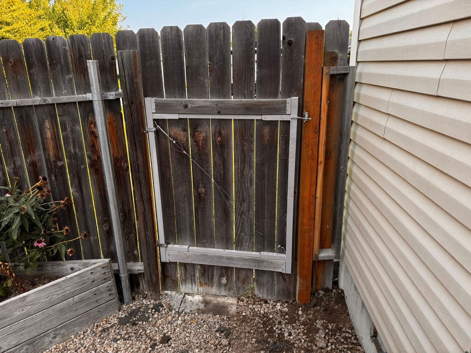 A weathered wooden fence with a gate, next to a beige siding.
