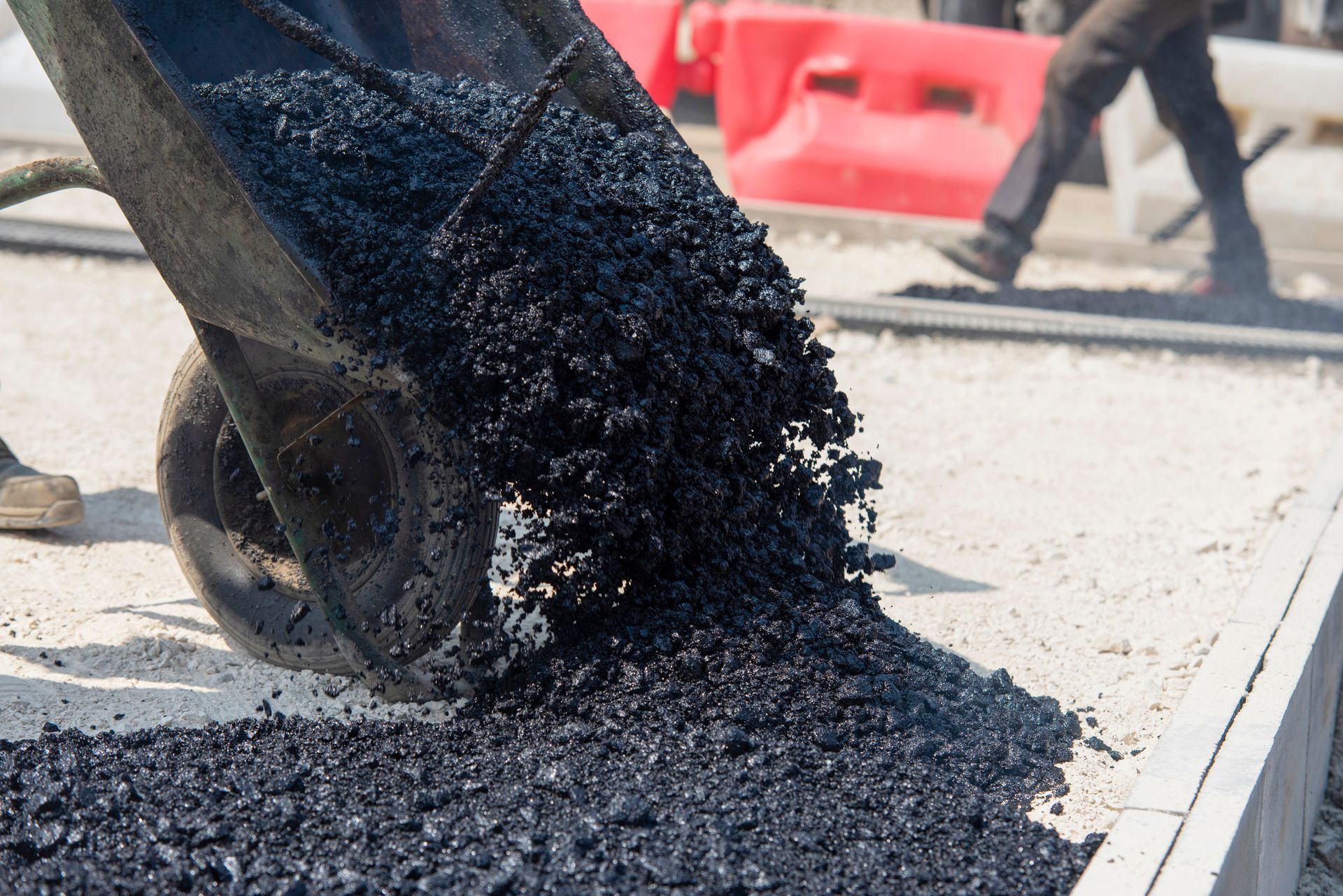 Excavator bucket dumping black asphalt onto a road surface during paving work