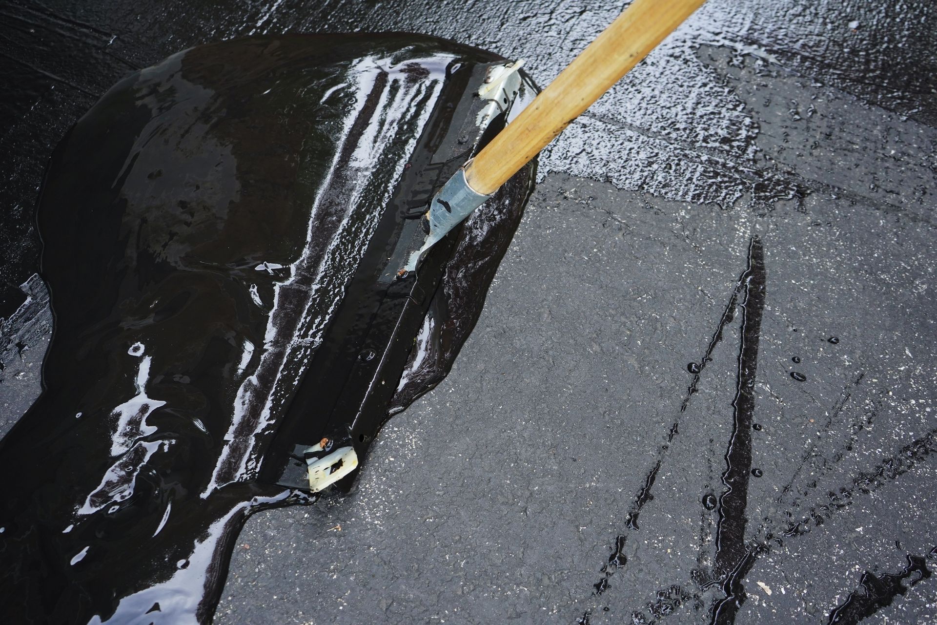 Shiny black puddle on dark pavement being scraped with a wooden stick Shiny black puddle on dark pavement being scraped with a wooden stick
