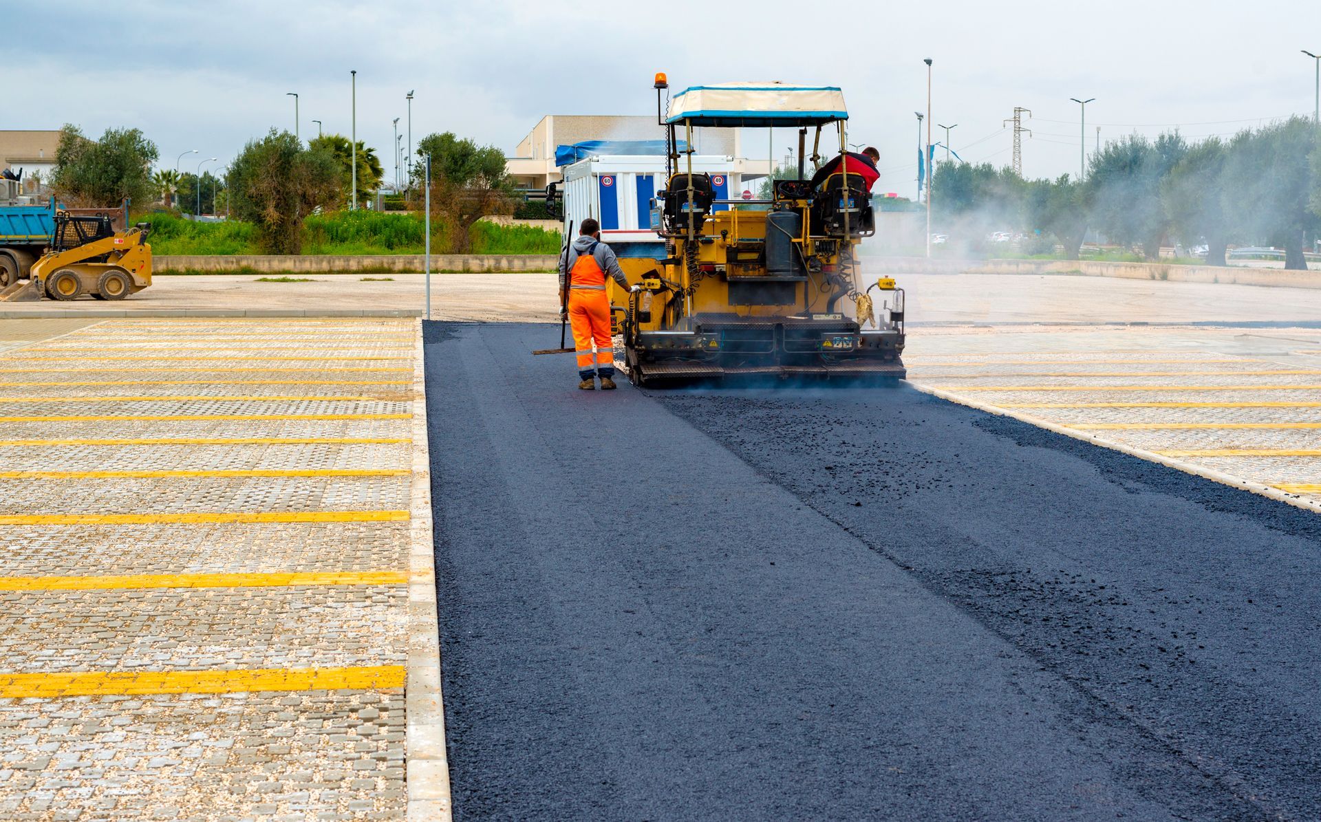 Road construction crew paving a new black asphalt lane beside a striped concrete road