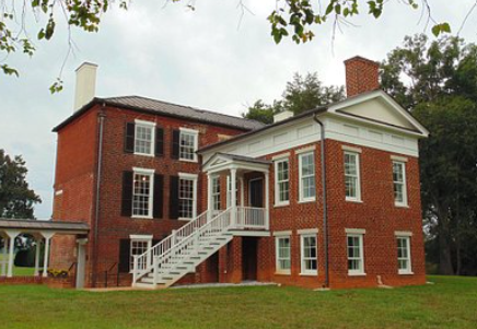 Red-brick historic house with white columns and exterior staircase on a grassy lawn Red-brick historic house with white columns and exterior staircase on a grassy lawn