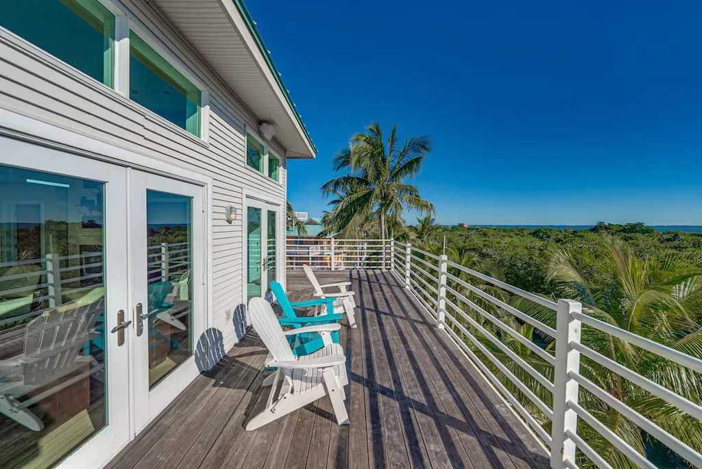 White house deck with Adirondack chairs overlooking a lush green landscape and blue sky.