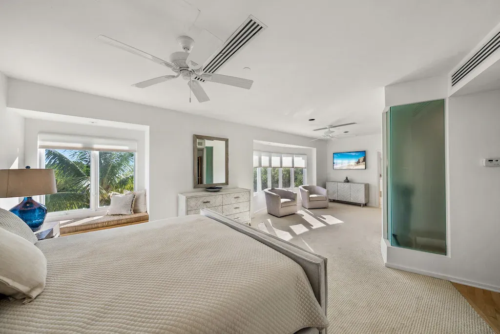 Bright, airy bedroom with a king-sized bed, window seat, and sitting area; all in shades of white.