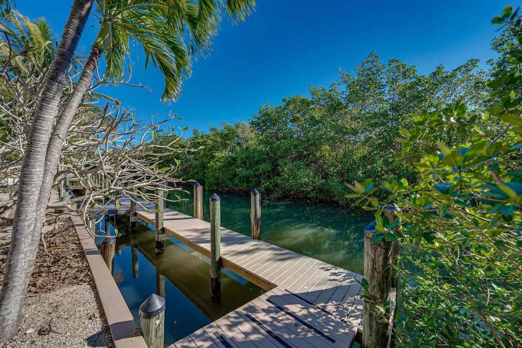 Wooden dock extending over a canal, flanked by trees and mangroves under a clear blue sky.