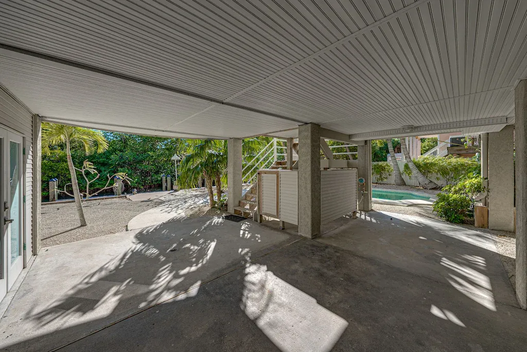 Covered patio with concrete columns and ceiling. Palm trees in the background, with a pool visible.