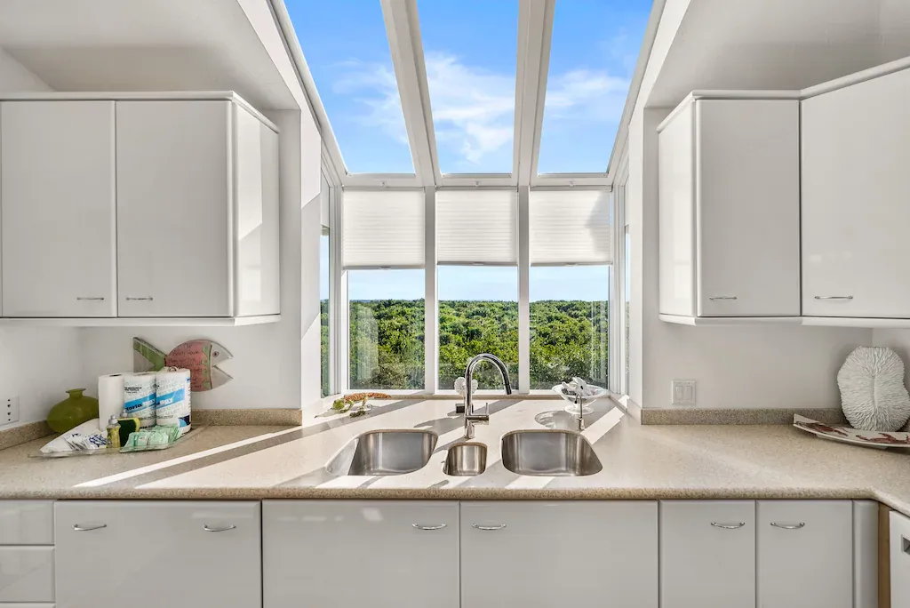 White kitchen with a view of trees and sky through a large window.
