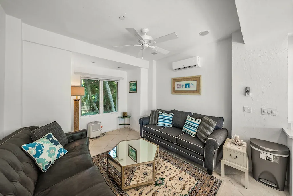 Living room with gray sofas, a mirrored coffee table, and colorful pillows.