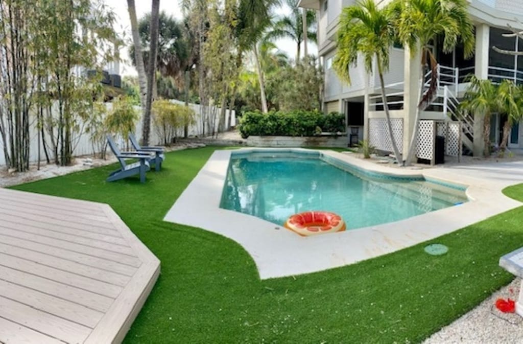 Backyard with a pool, artificial turf, and a house. The pool has a floating device.