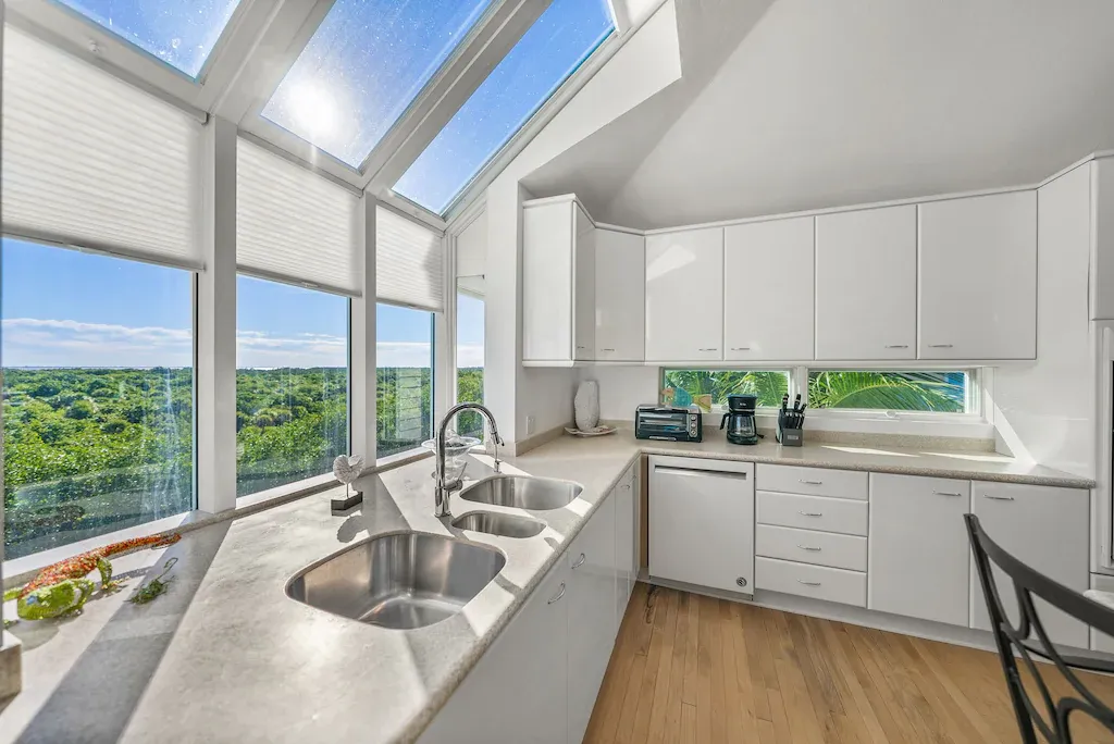 White modern kitchen with large windows overlooking a green landscape.