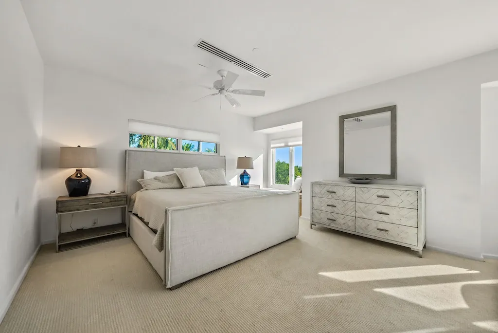 Bedroom with white walls, bed, dresser, mirror, and large window.