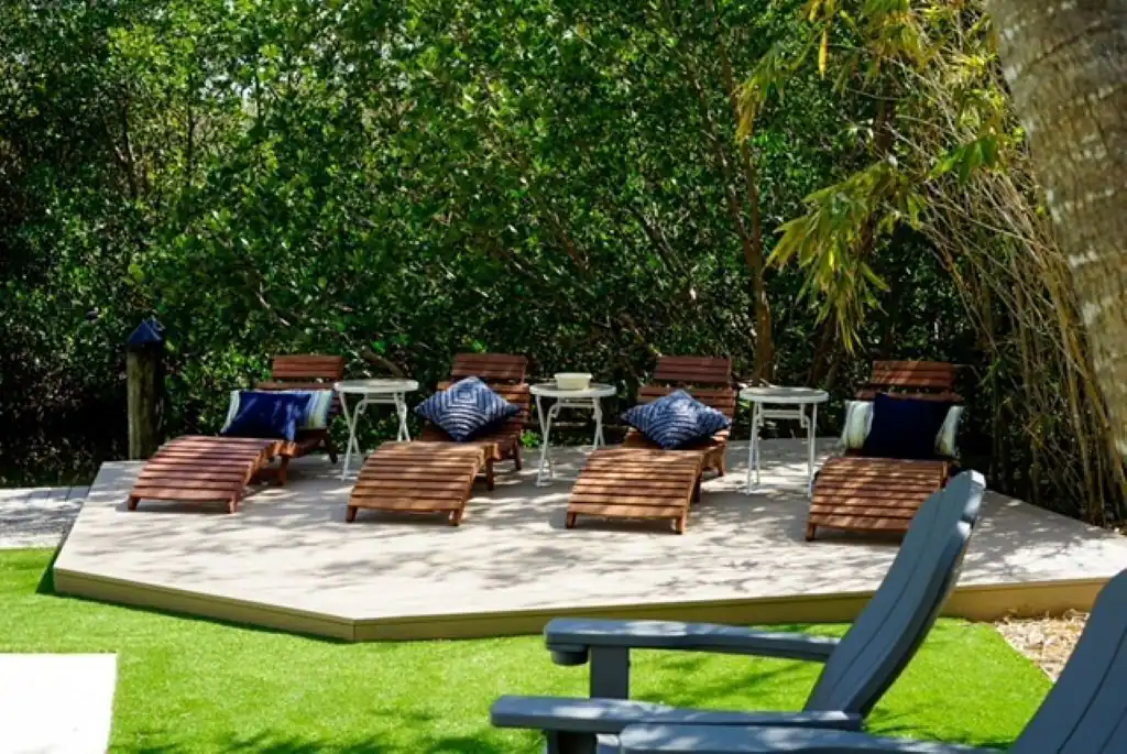 Lounge chairs on a concrete patio surrounded by greenery, with blue cushions, sunny outdoor setting.